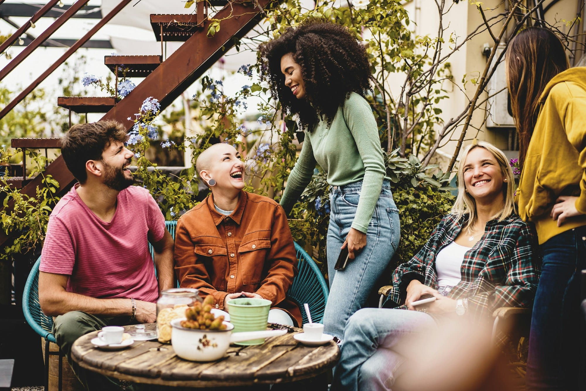 Multiethnic generation z people gathering in the hostel terrace drinking coffee and talking together